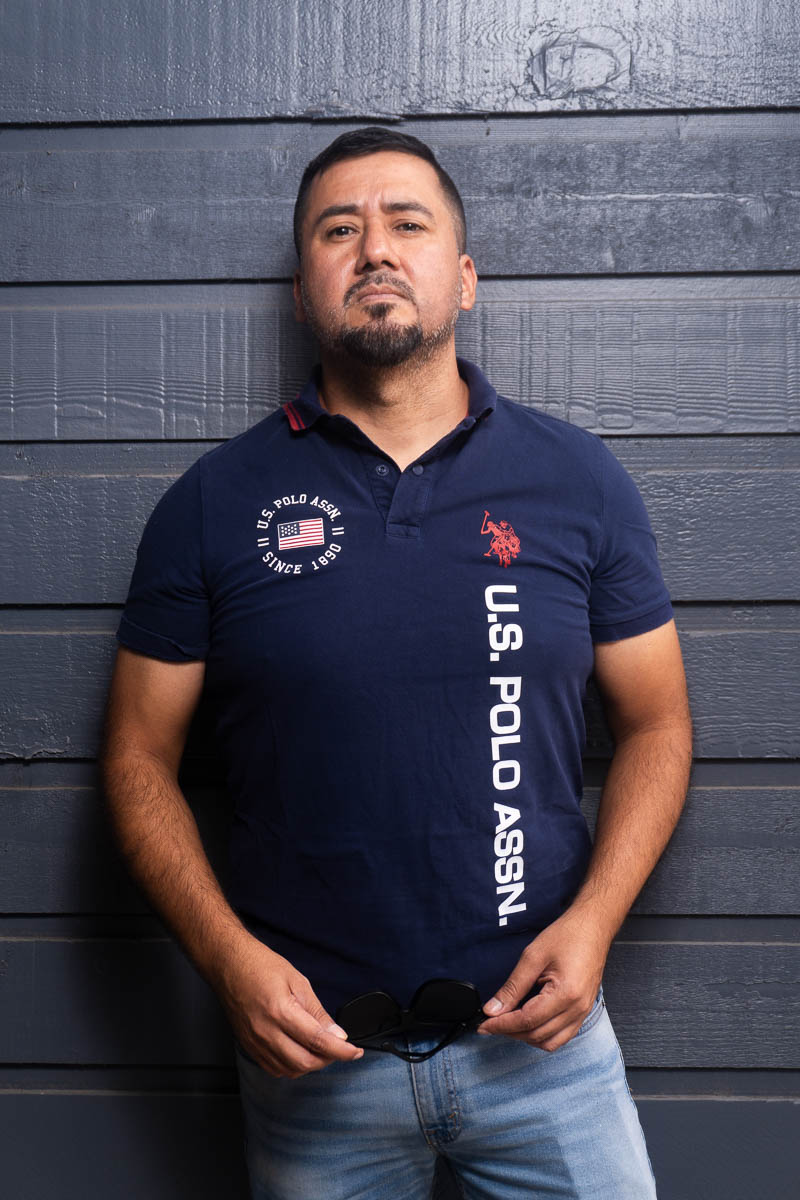 Portrait of Cesar, looking at the camera wearing a dark blue polo shirt and denim pants.