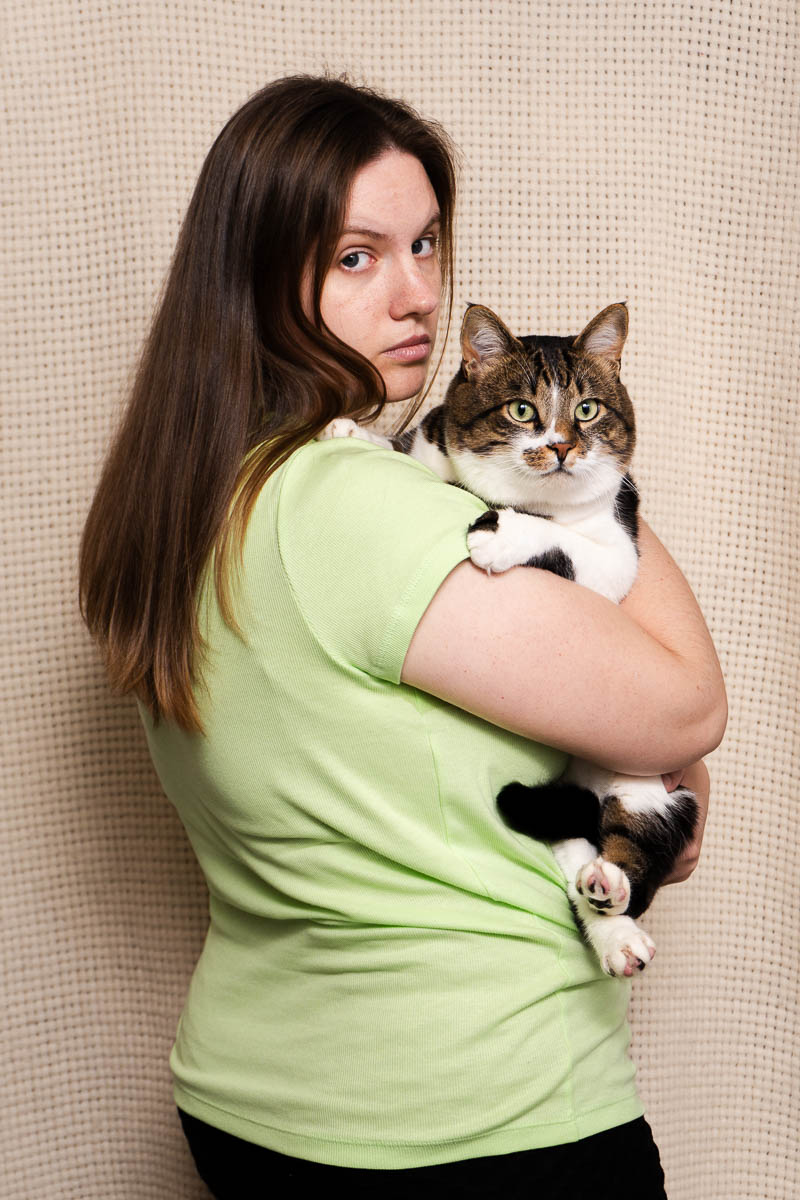 Portrait of Hanna, on her back facing the camera holding a cat and is wearing a mint green t-shirt.