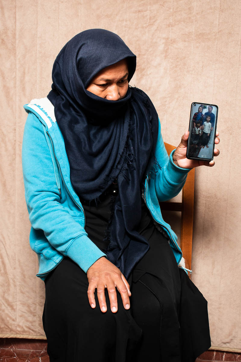 Portrait of Rozima, hiding her face and holding a cellphone with persons in it,