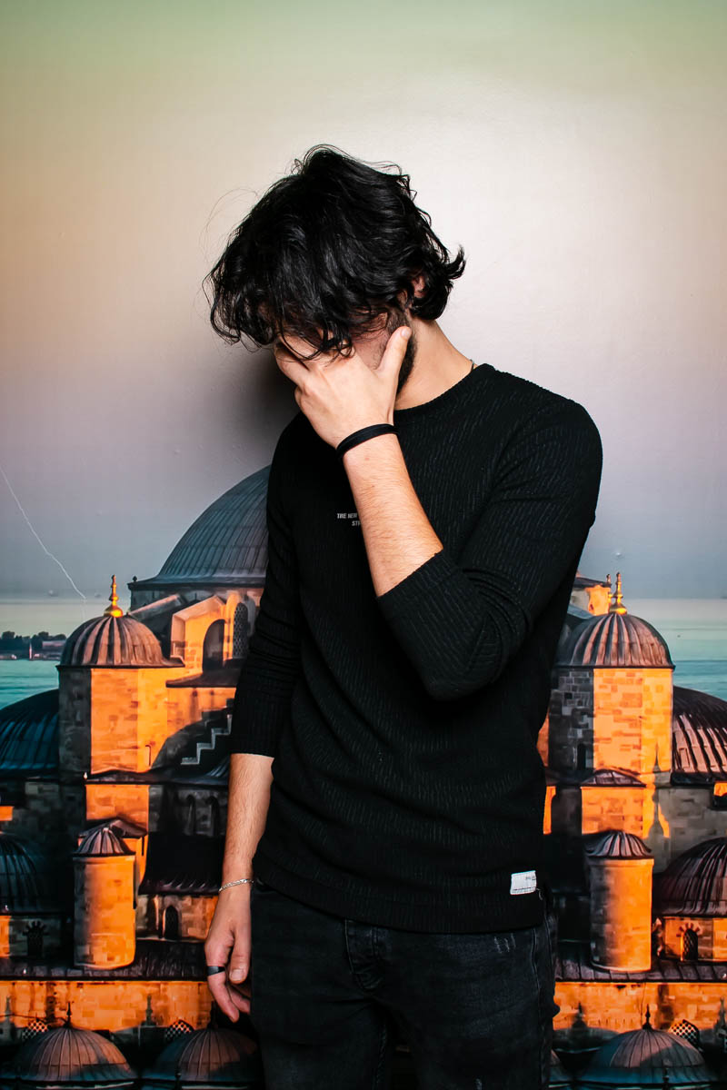 Portrait of Moaz, wearing a black long sleeves covering his face with his hands.