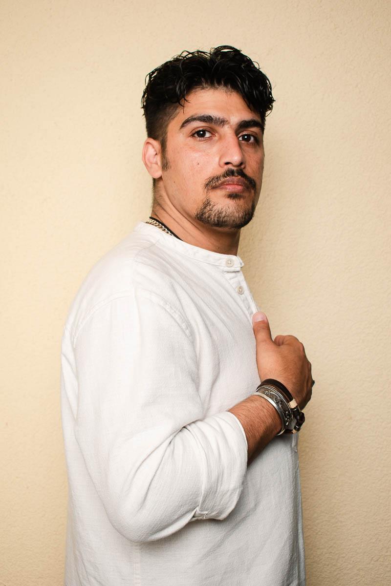 Portrait of Mojtaba, facing sideward, hands on chest and wearing a white long sleeves.