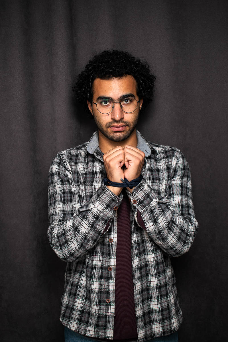 Portrait of Ammar, both hands clasped in chest wearing a striped polo and is looking at the camera in a neutral way.