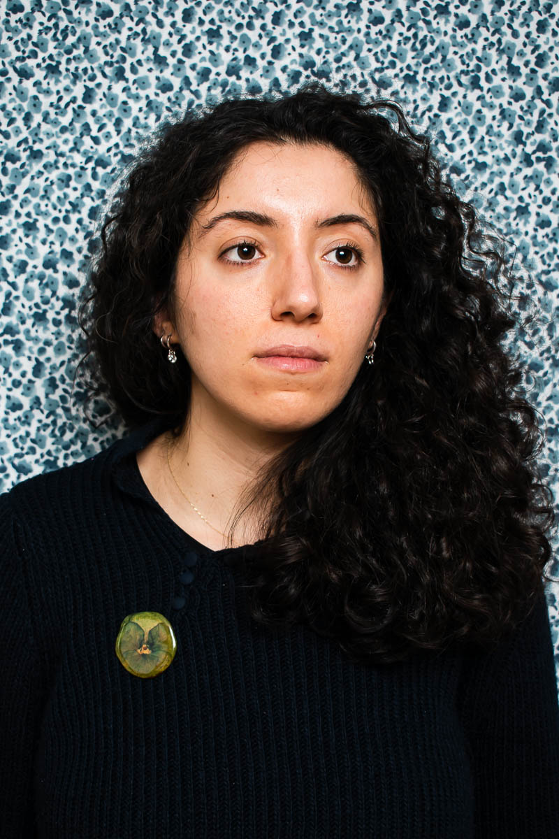 Portrait of Rojbin, looking at the other side from the camera wearing a black shirt and has curly hair.