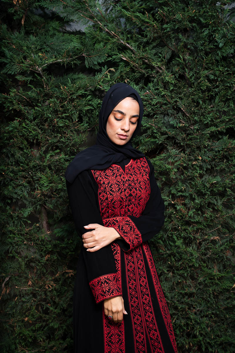 Portrait of Hadeel, facing downward and not looking to the camera, wearing a red and black dress with a hijab.