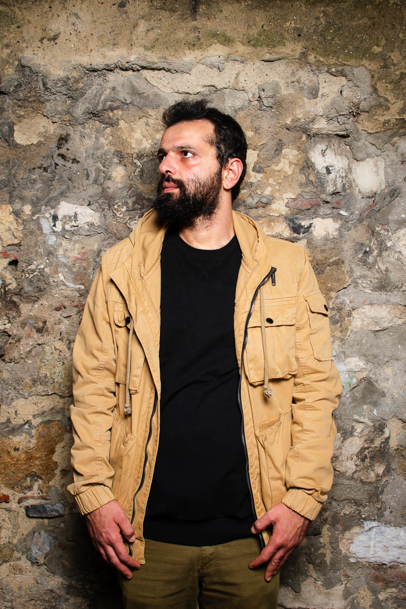 Portrait of Ayham, not looking directly into the camera and is wearing a yellow orange jacket with a black shirt underneath.