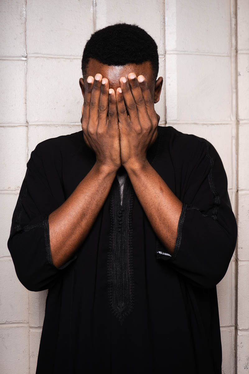 Portrait of Elhadj, covered his face using his hands and is wearing a black jacket.