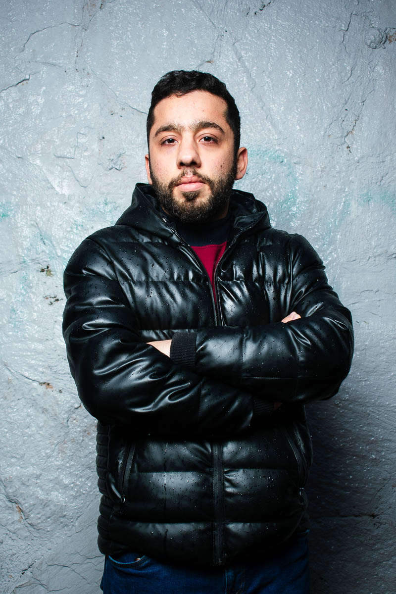 Portrait of Mahmod, arms clasped together and is wearing a dark leather jacket.