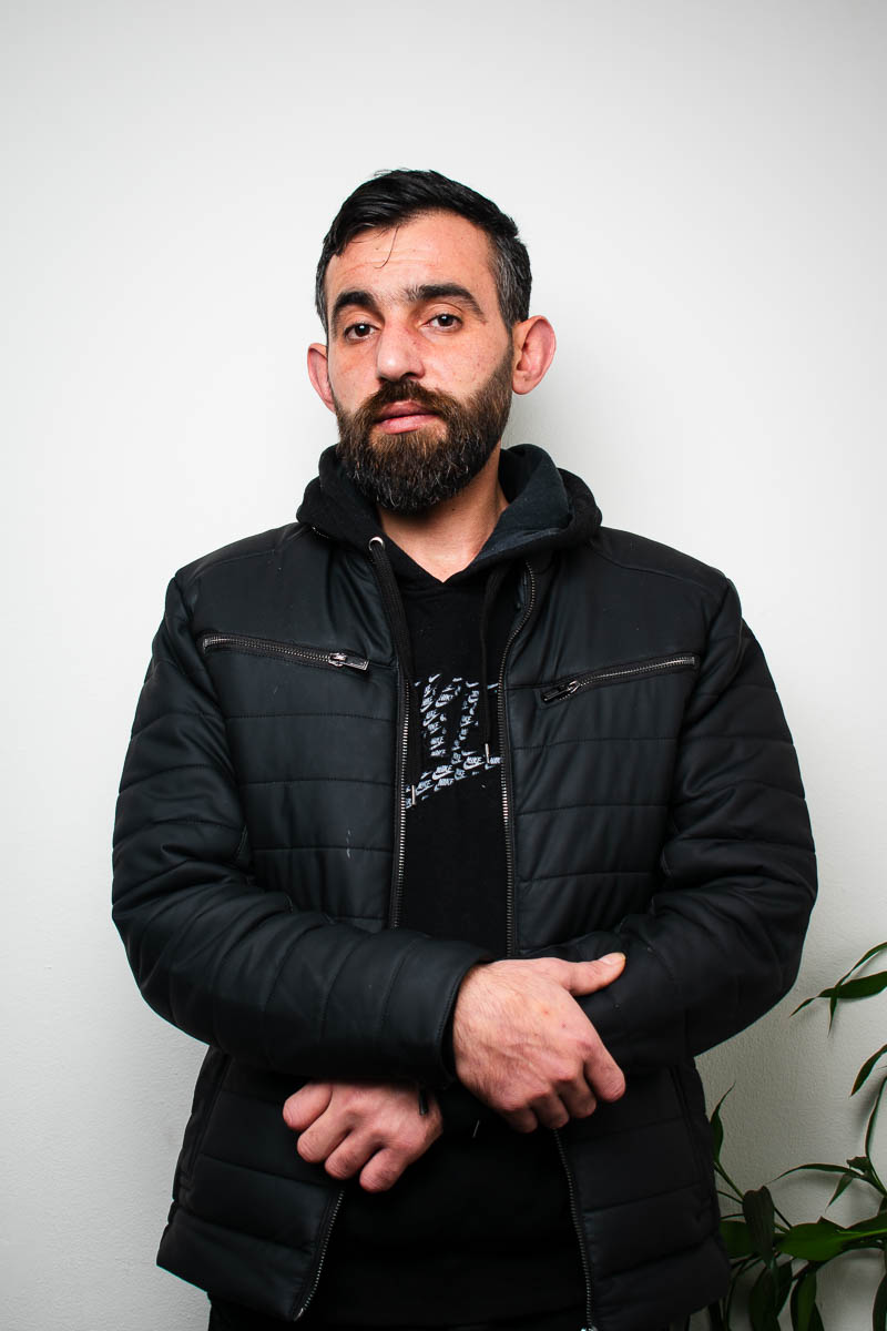 Portrait of Majed, hands clasped together and is wearing a black leather jacket.
