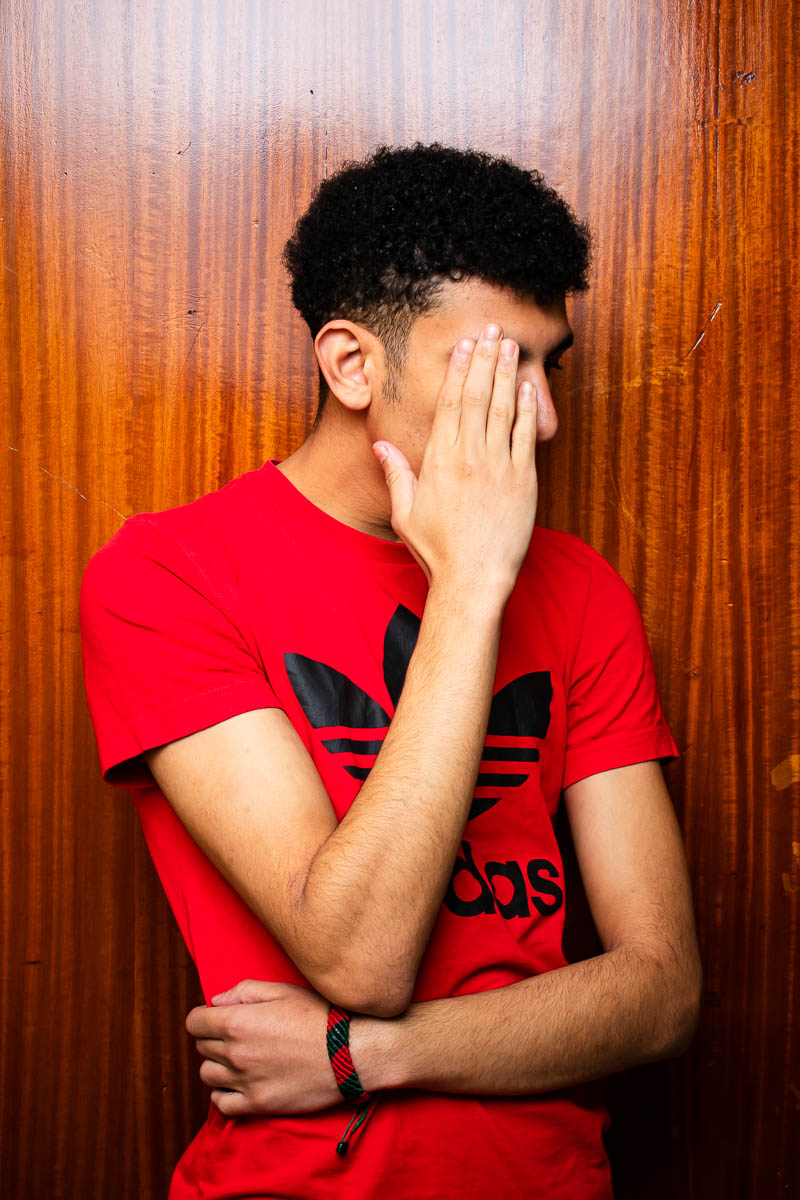Portrait of Mouad, covering his face to the camera and is wearing a red shirt.