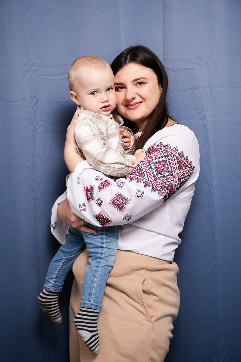 Portrait of Viktoriia, smiling at the camera and is holding a baby.