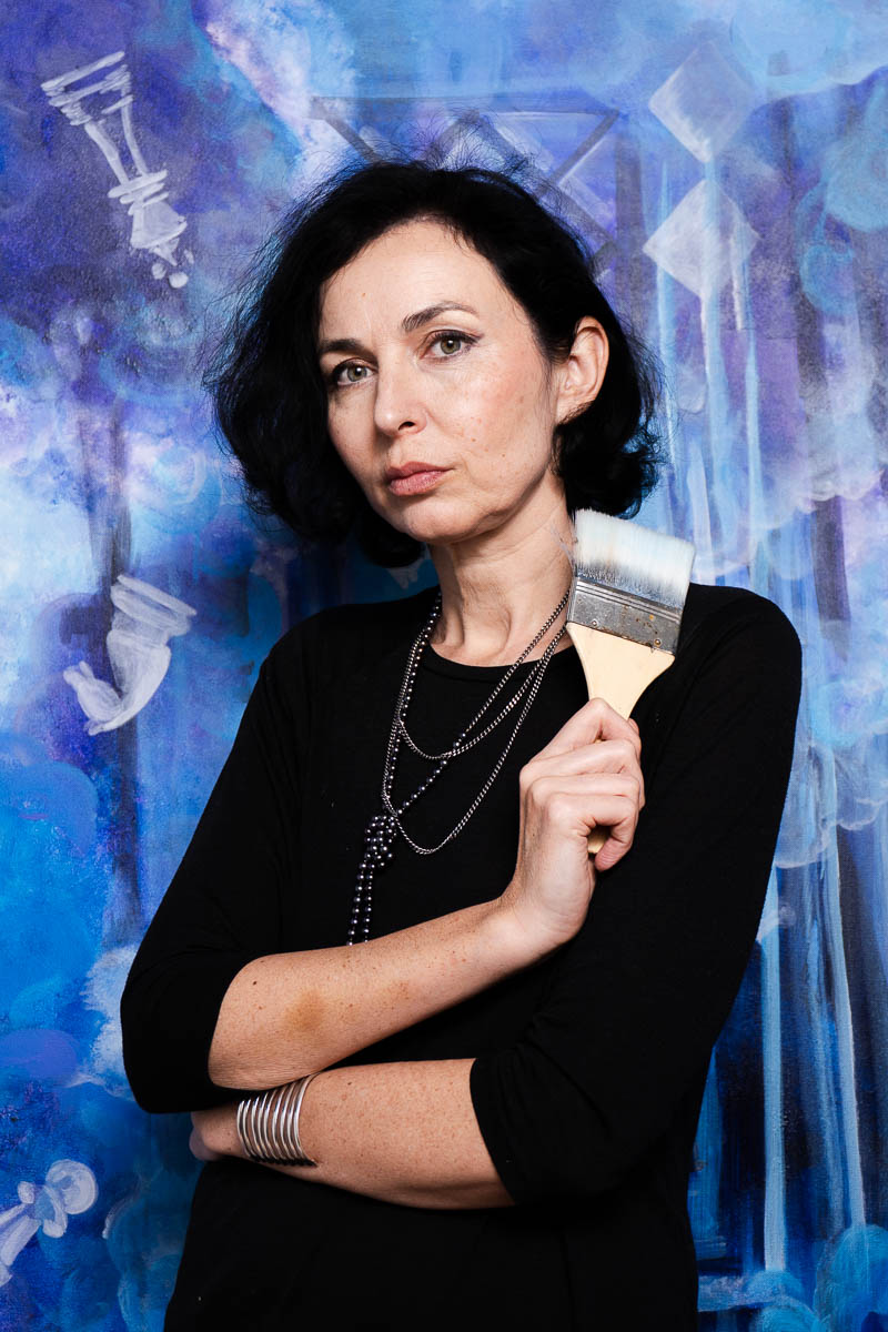 Portrait of Yana, looking at the camera and is holding a paintbrush.