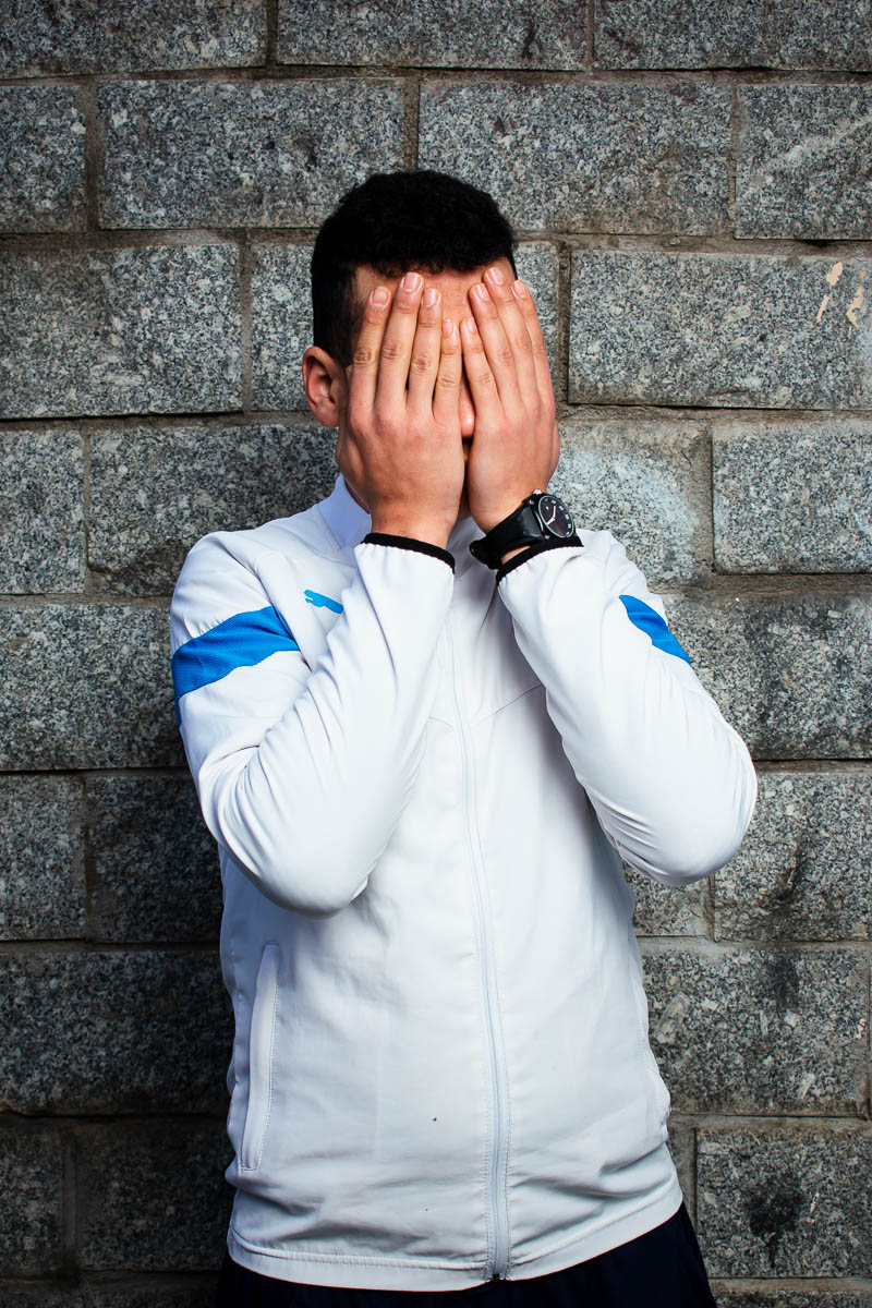 Portrait of Oussama, covered his face with his hands and is wearing a white jacket.
