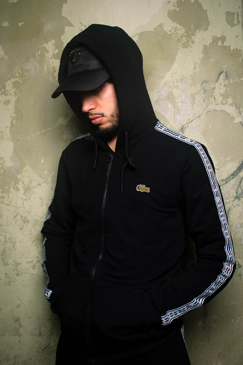 Portrait of Taitai, not showing his face to the camera and is wearing a black jacket and a black cap.