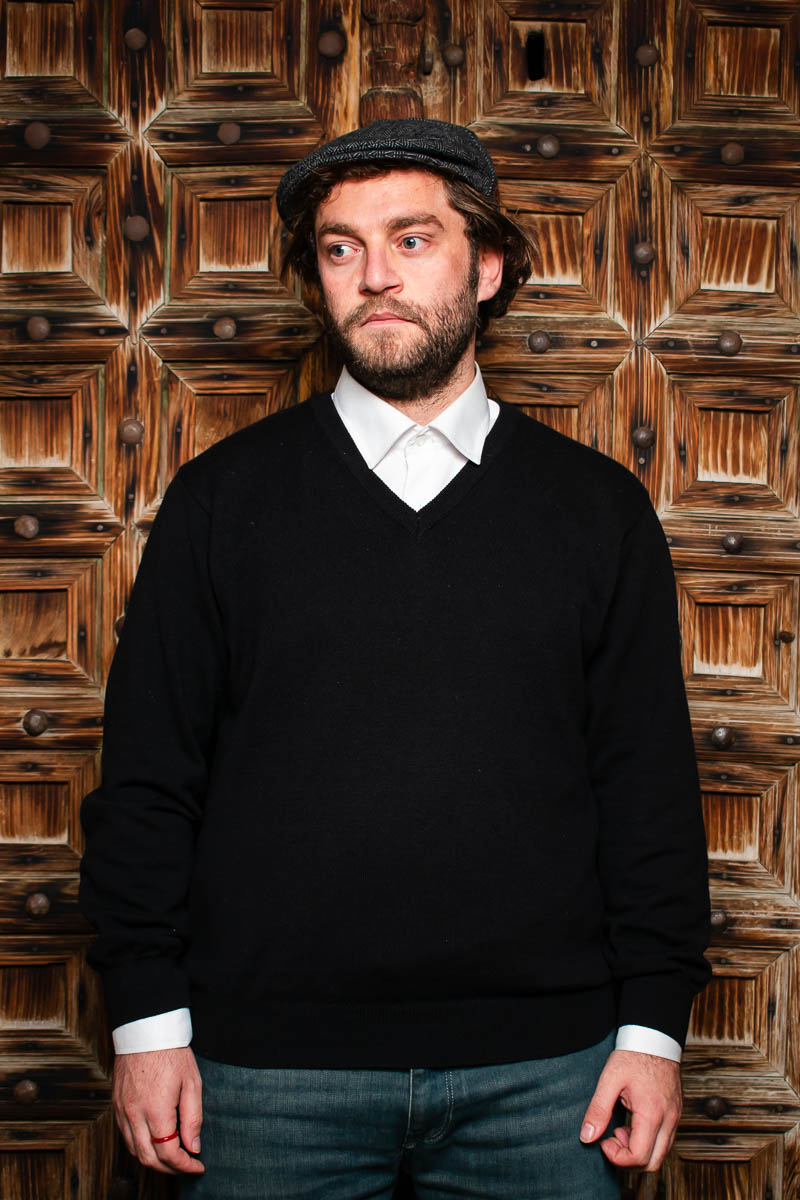 Portrait of Hasan, facing sideways wearing a black long sleeves with white polo underneath.