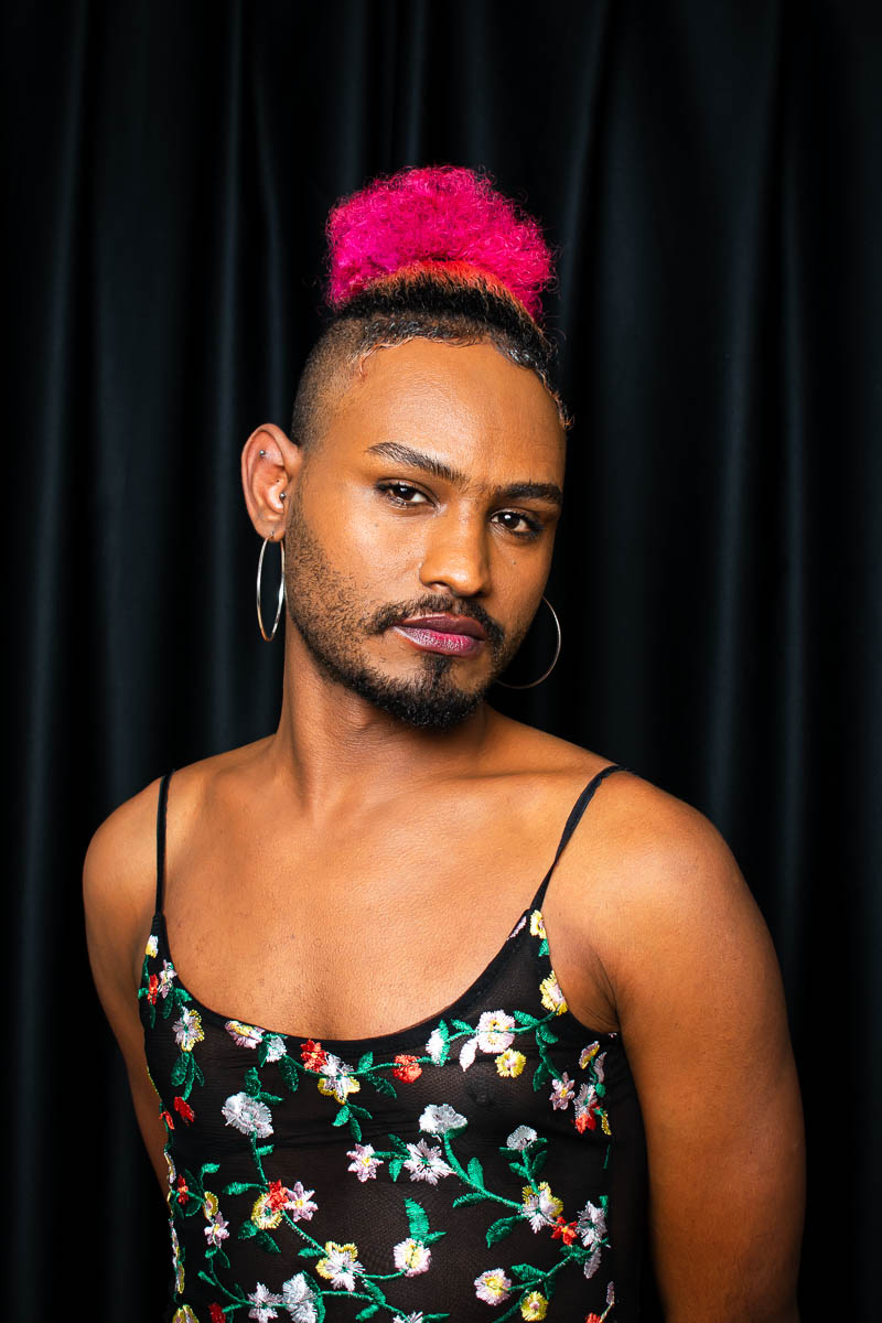 Portrait of Mujja, wearing a pink headband and a floral sleeveless, while looking intently at the camera.