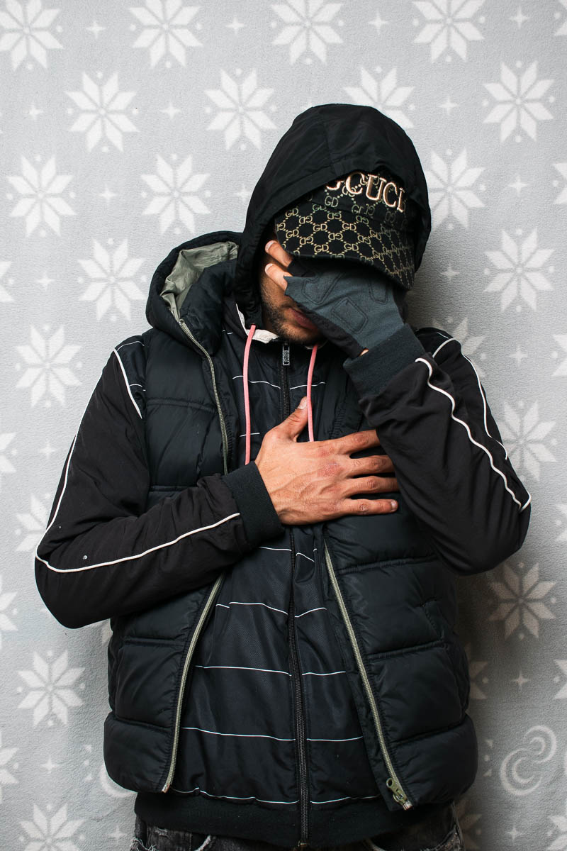 Portrait of Ibra, covered his face using his hands and is wearing black jacket and a gucci hat.
