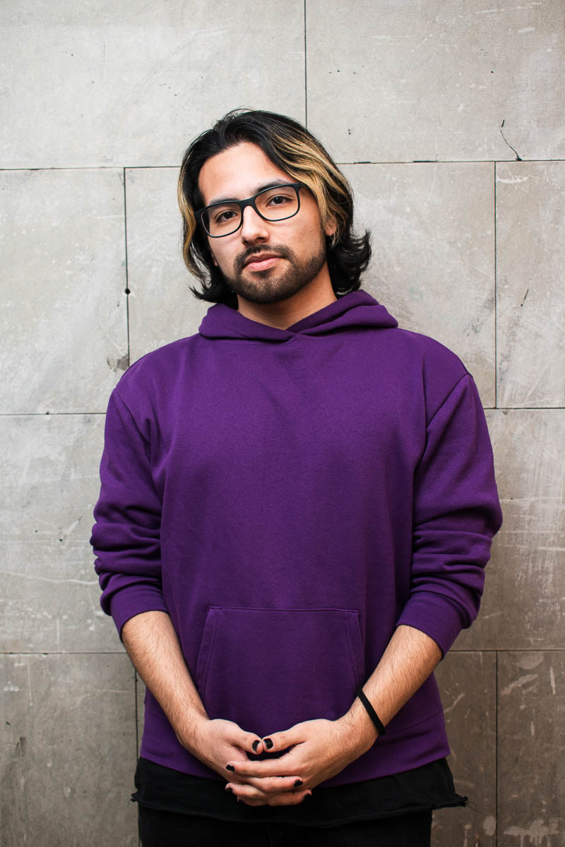 Portrait of Daniel, facing the camera, hands clasped together and is wearing a purple jacket.