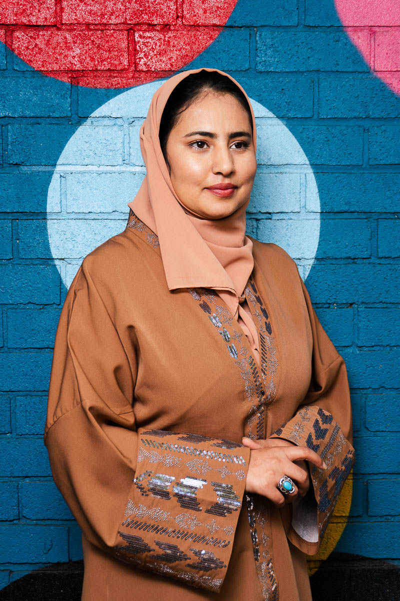 Portrait of Ayat, facing sideways and is wearing a brown dress and a scarf.