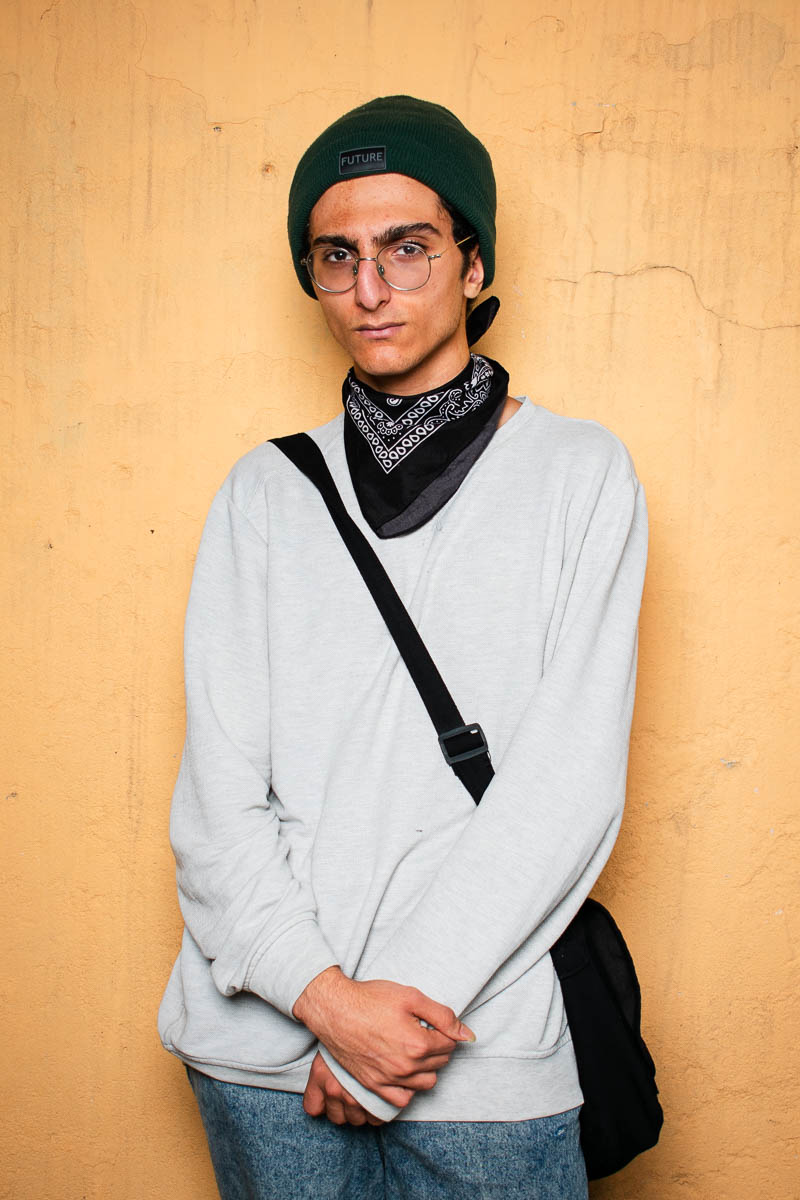 Portrait of Saeed, looking intently at the camera, hands clasped and is wearing a white long sleeves and a black shoulder bag.