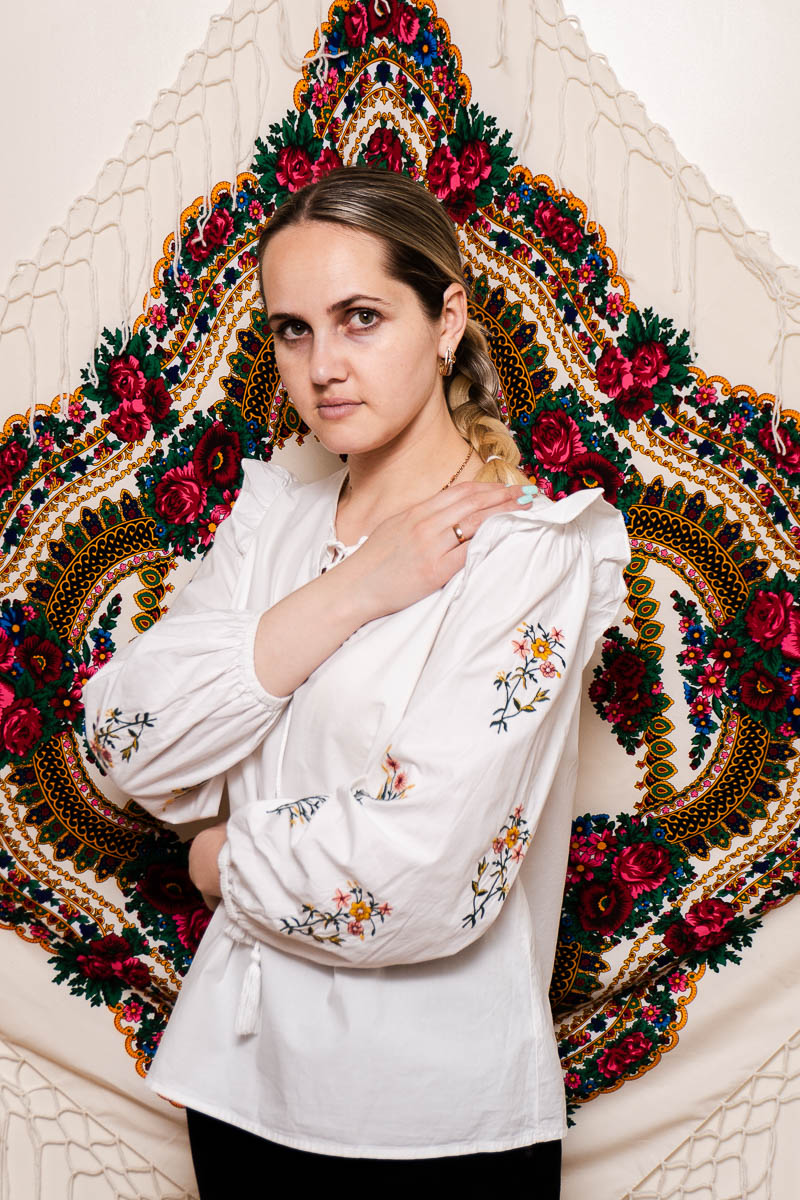 Portrait of Khrystyna, looking intently in the camera and is wearing a white floral long sleeves.
