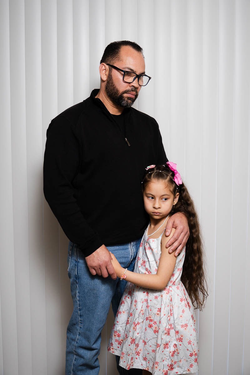 Portrait of Nelson, wearing a black long sleeves with eyeglasses and is holding a young girl.