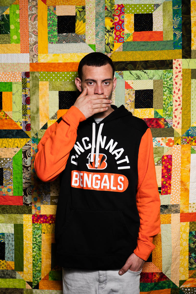 Portrait of Israel,covered his mouth using his hand and is wearing a jacket in orange and black print.