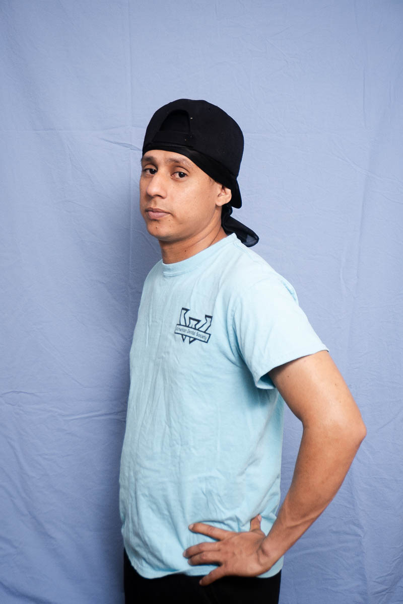 Portrait of Yordin, facing sideways, hands on hips and is wearing a light blue shirt.