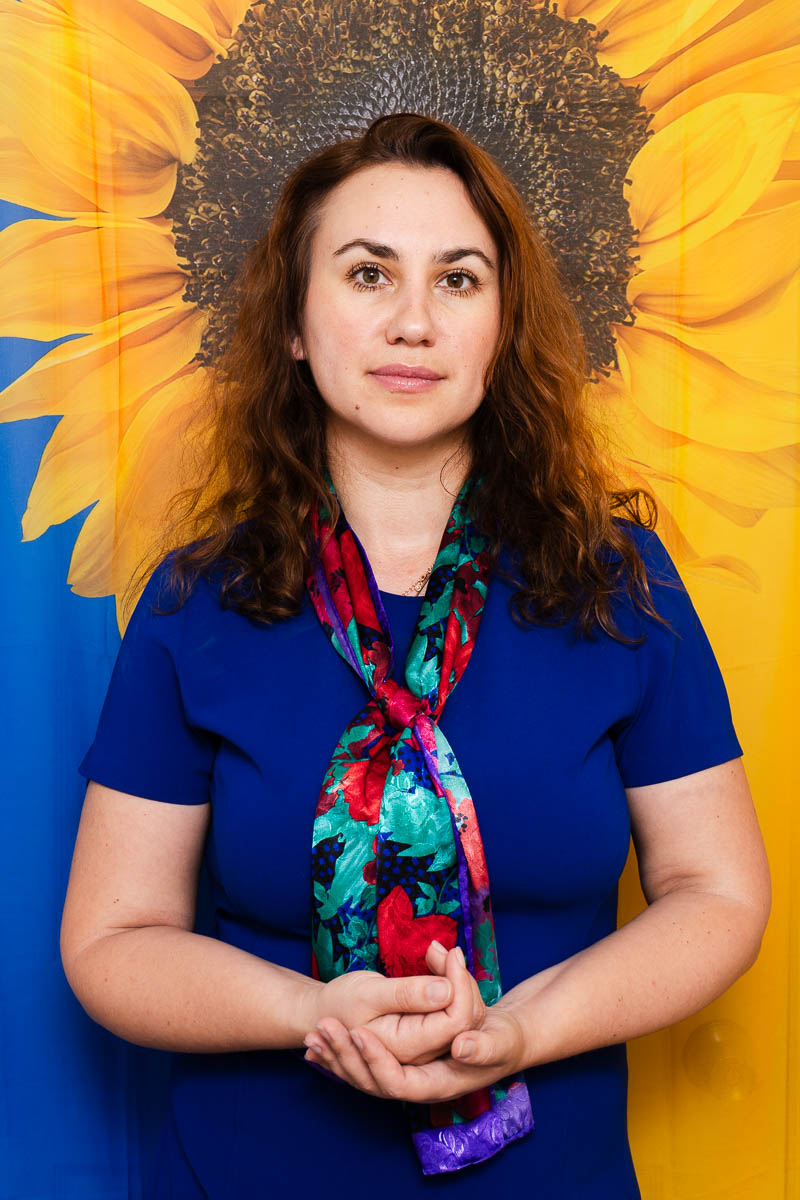 Portrait of Olha, wearing a blue shirt and a scarf.