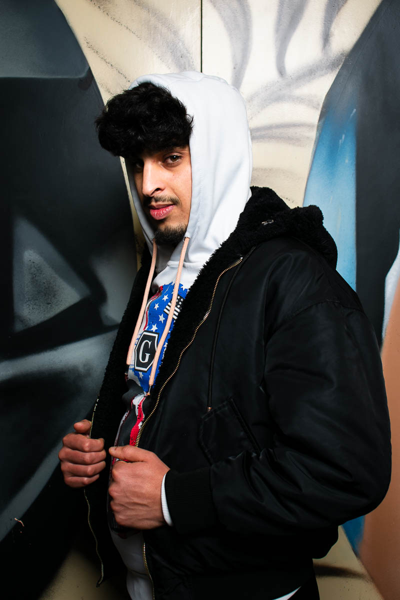 Portrait of Imad, wearing a black jacket with hoodie and is looking at the camera.